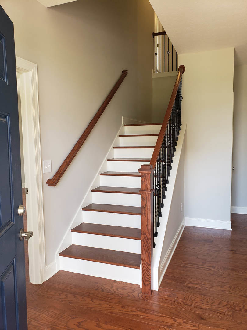 White and brown staircase with wooden handrail and balusters, hardwood floor, blue door, and adjacent wood shelving in a modern interior