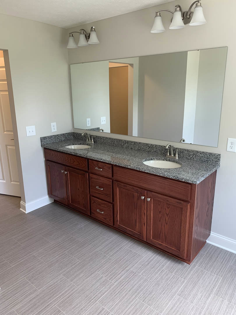 Bathroom with granite countertop, double sinks, white cabinetry, large wall mirror, and three-lamp light fixture above sinks