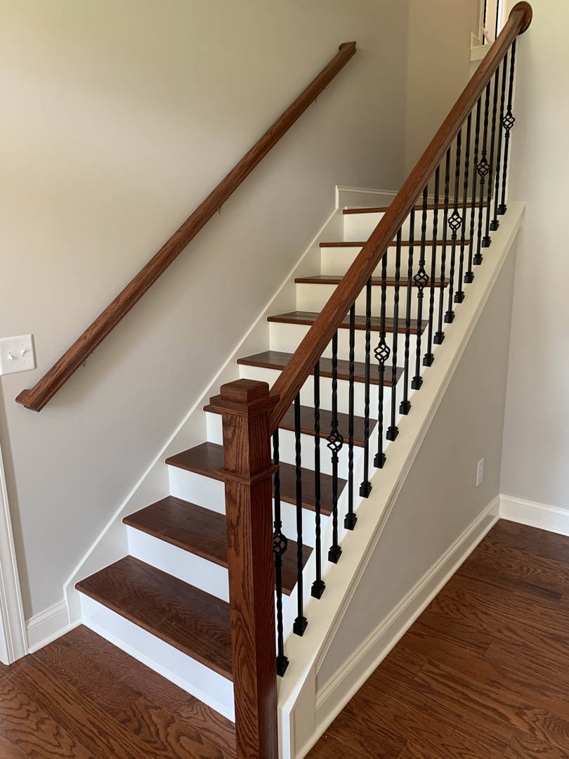 Staircase with hardwood steps, wood handrails, and metal balusters, adjacent to a white wall with a double light switch