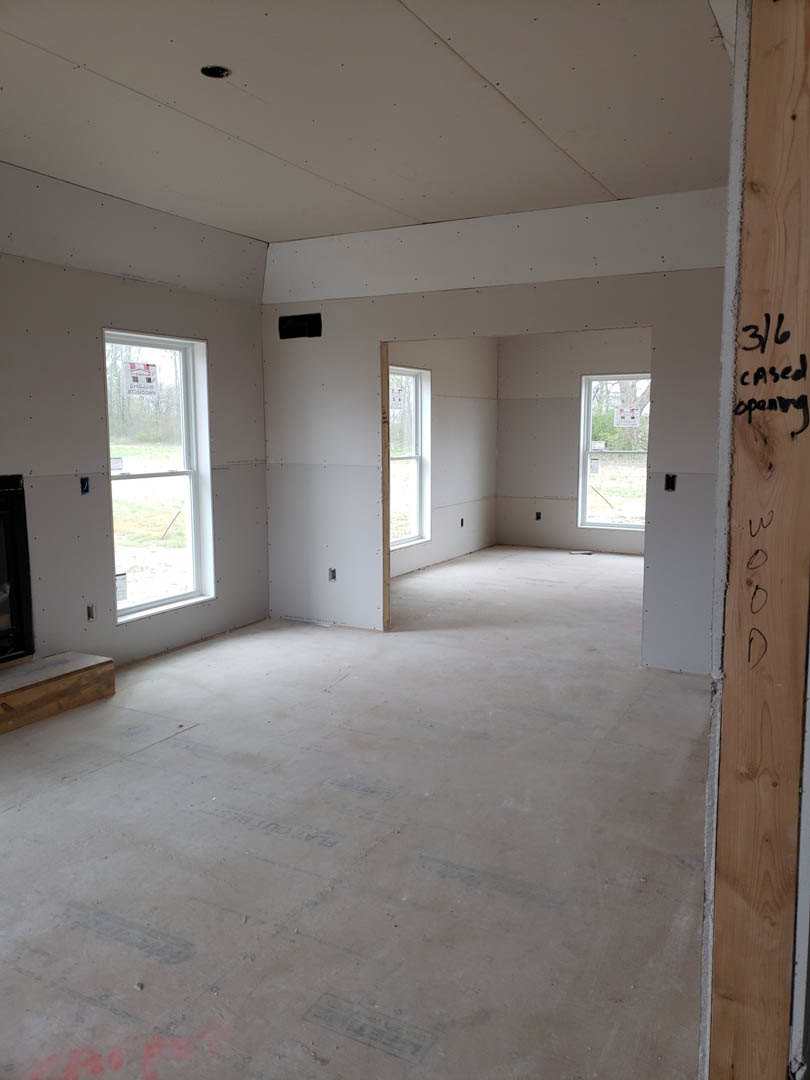 Living room with large windows, white trim, stone fireplace, light wood flooring, and neutral plaster walls