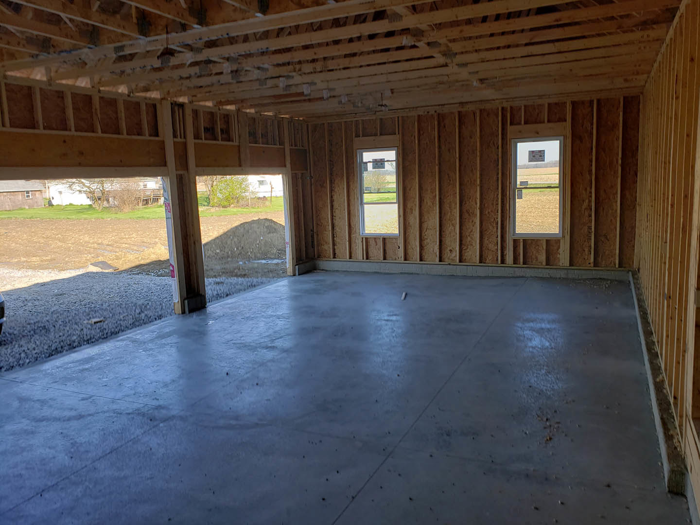 Spacious room featuring large windows, exposed wood framing, and smooth concrete flooring