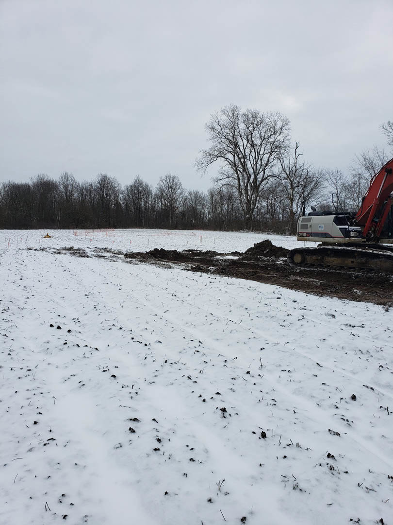 Yellow bulldozer parked on snow-covered field, leafless trees in background, overcast winter sky