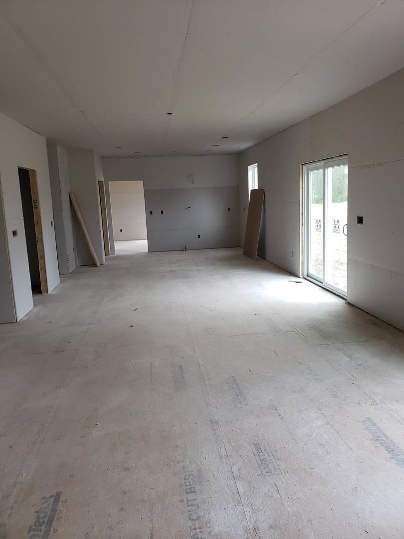 Modern interior room featuring a large black-framed window, white plaster walls, black door with matching handle, light wood flooring, and a wooden accent stick mounted on the
