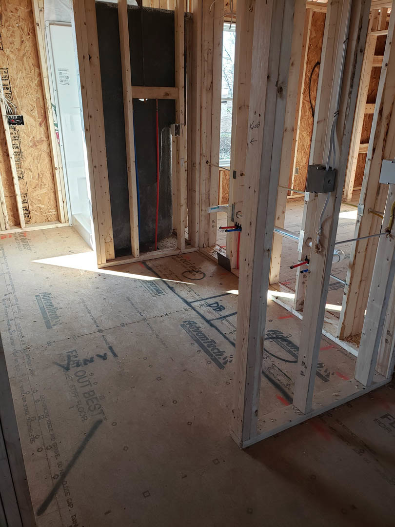 Unfinished room with exposed wood framing, door opening, window, red and blue plumbing pipes, electrical wires, and black electrical box mounted on wall