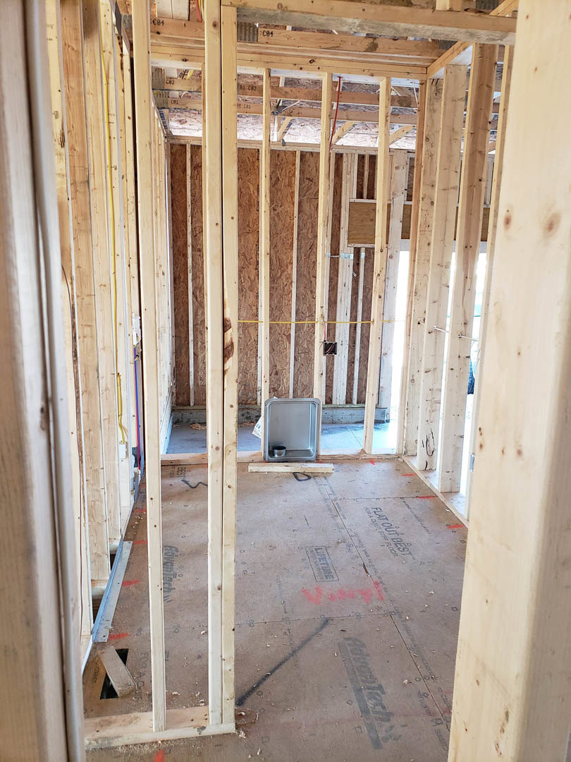 Living space with exposed wood ceiling beams, light-colored wood flooring, and a rectangular metal box placed on the floor.