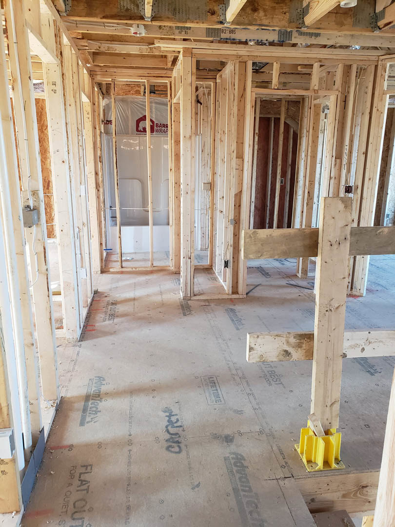 Room under construction with exposed wood framing, yellow plastic insulation, and a white shower stall surrounded by wooden planks.