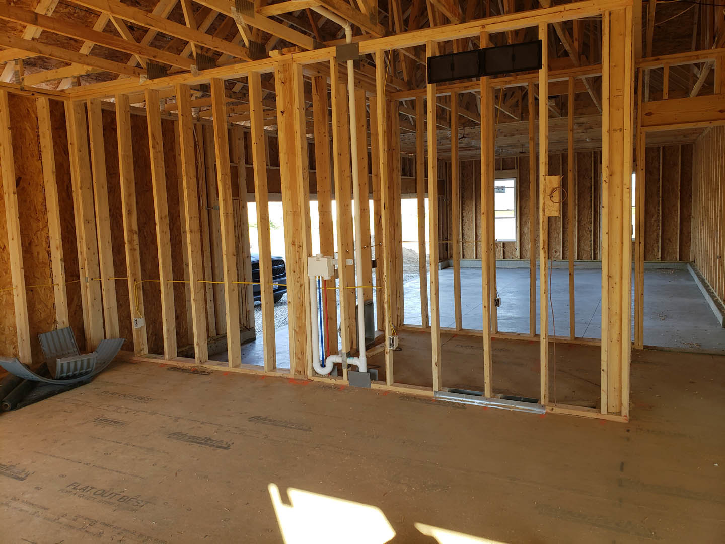 Exposed wood framing with ceiling beams, unfinished floor, visible plumbing pipes, and construction insulation in a partially built residential interior