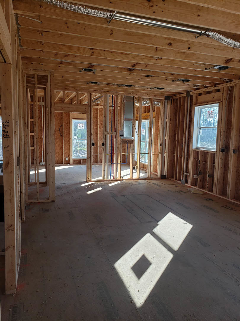 Living room with exposed wood ceiling beams, large windows overlooking water and trees, light-colored walls, and visible metal pipe along the ceiling.
