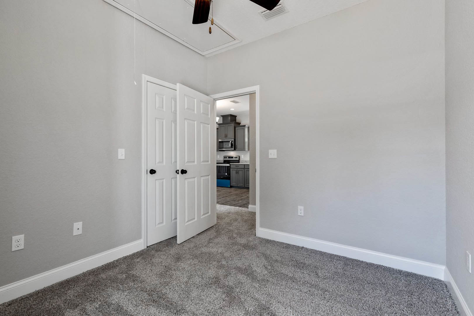 Carpeted room with white walls, ceiling fan, two white doors, electrical outlet, and window