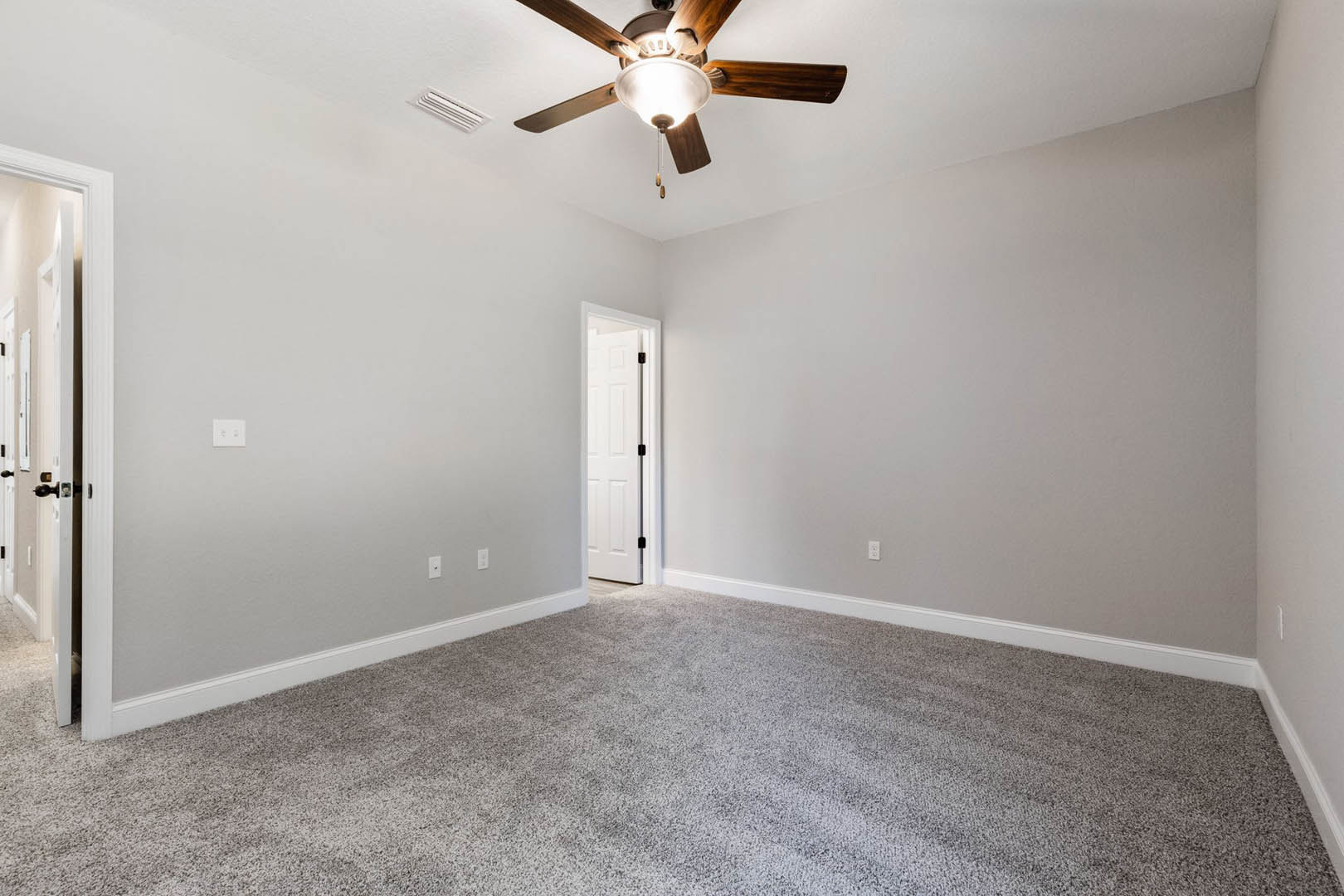 Ceiling fan with integrated light fixture above carpeted floor, white door with black handle, plaster walls, and crown molding