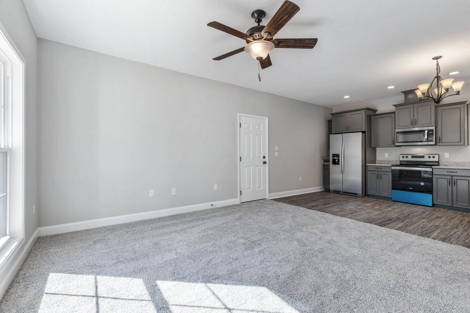 Open-concept room featuring a ceiling fan with light, stainless steel refrigerator, white cabinetry with black knobs, carpeted flooring, and a microwave on the countertop.
