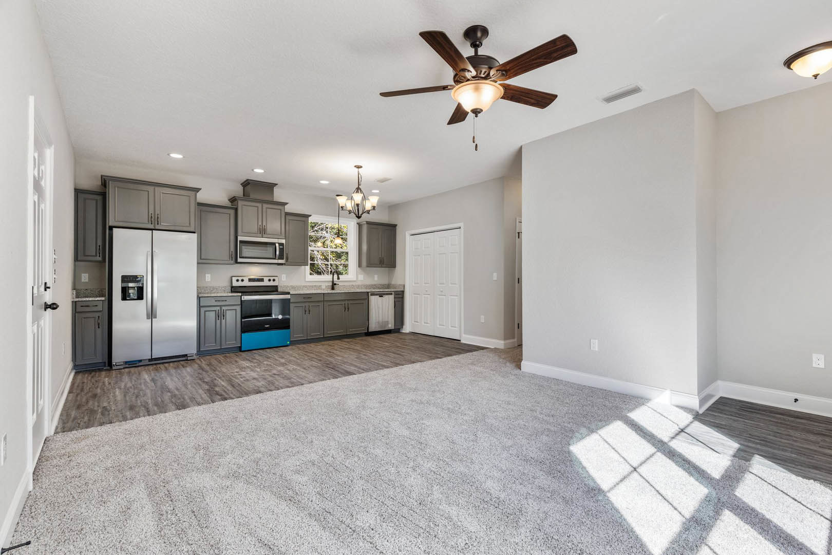 Open kitchen with stainless steel refrigerator, glass door stove, white cabinetry, and ceiling fan with light fixture; adjacent white door with black handle.