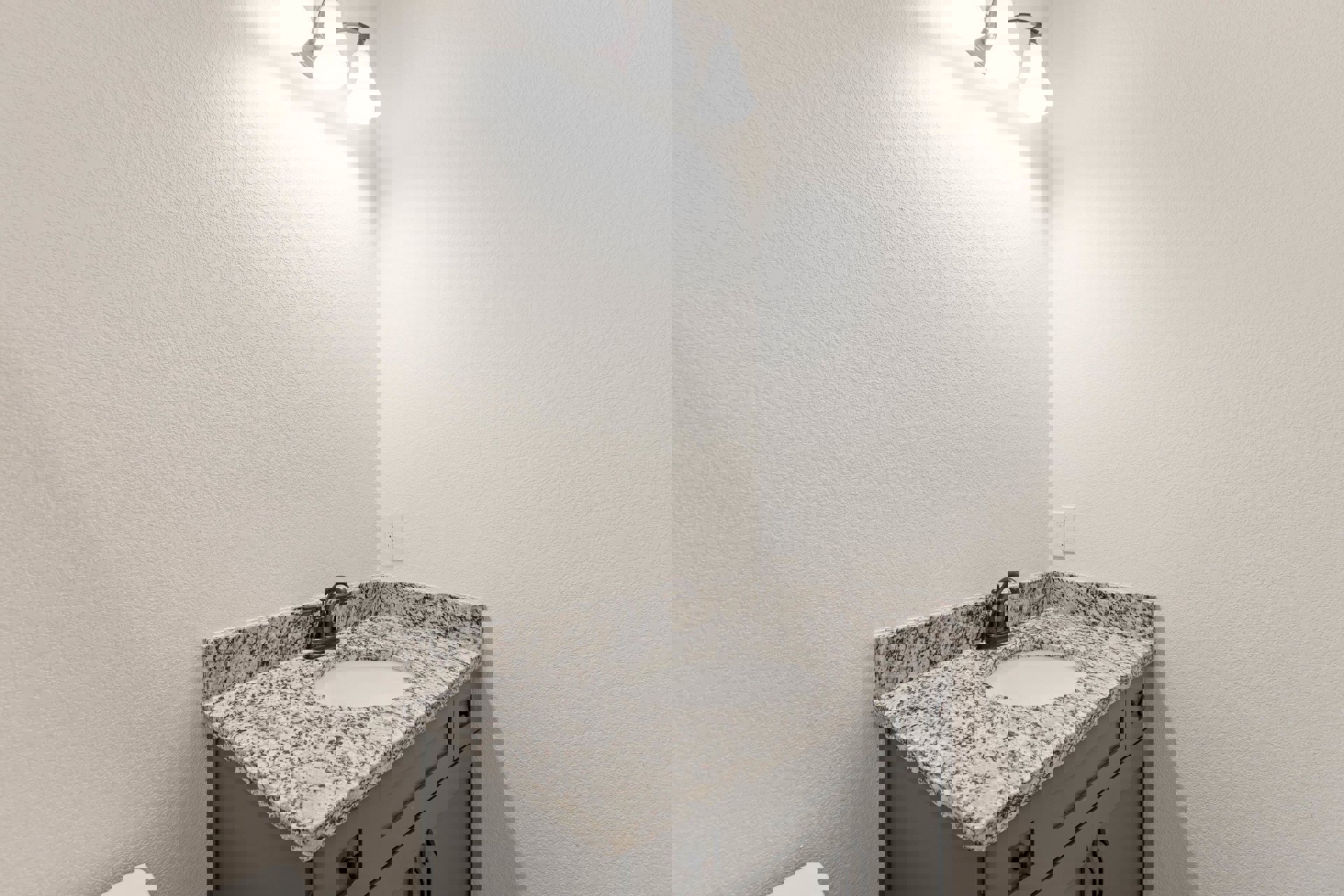 White sink with black speckled marble countertop, modern faucet, and tile backsplash in a bathroom with cabinetry and drawers