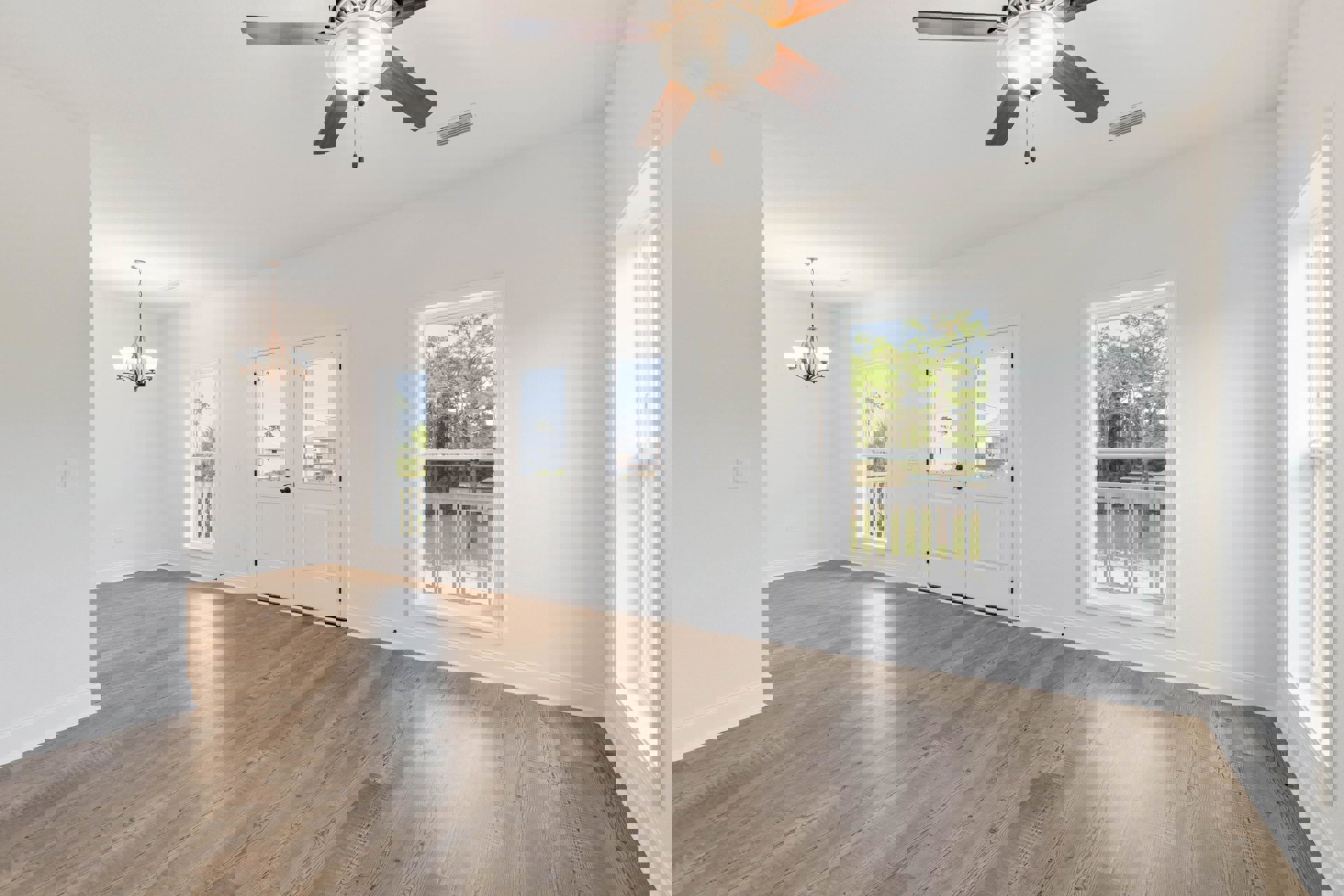 Ceiling fan with light fixture mounted on white ceiling, wood flooring, double glass doors, windows with white trim overlooking trees, white walls, close-up of chandelier.