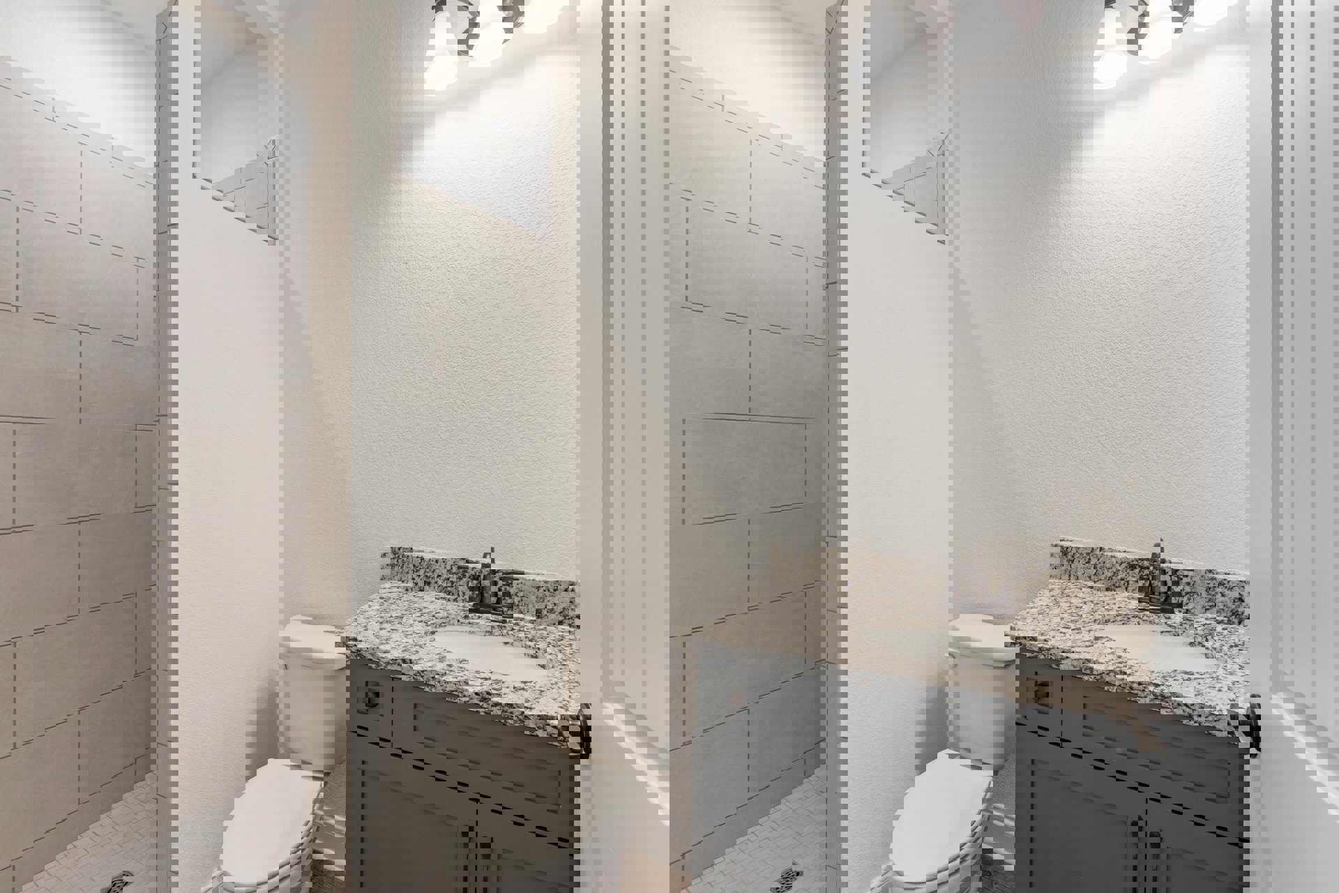 White toilet beside marble countertop vanity, chrome faucet, light gray tile floor, neutral painted walls