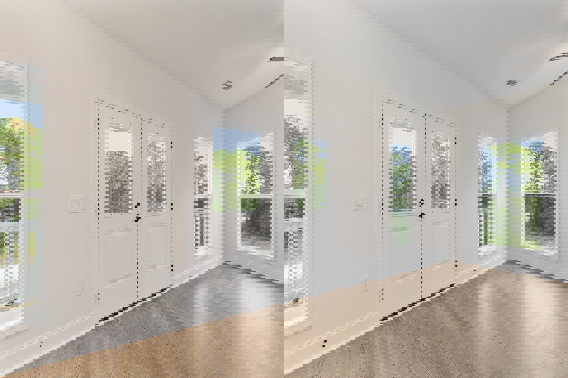 White double doors with modern hardware set in a room featuring light wood flooring, adjacent to a large window framing leafy trees outside.