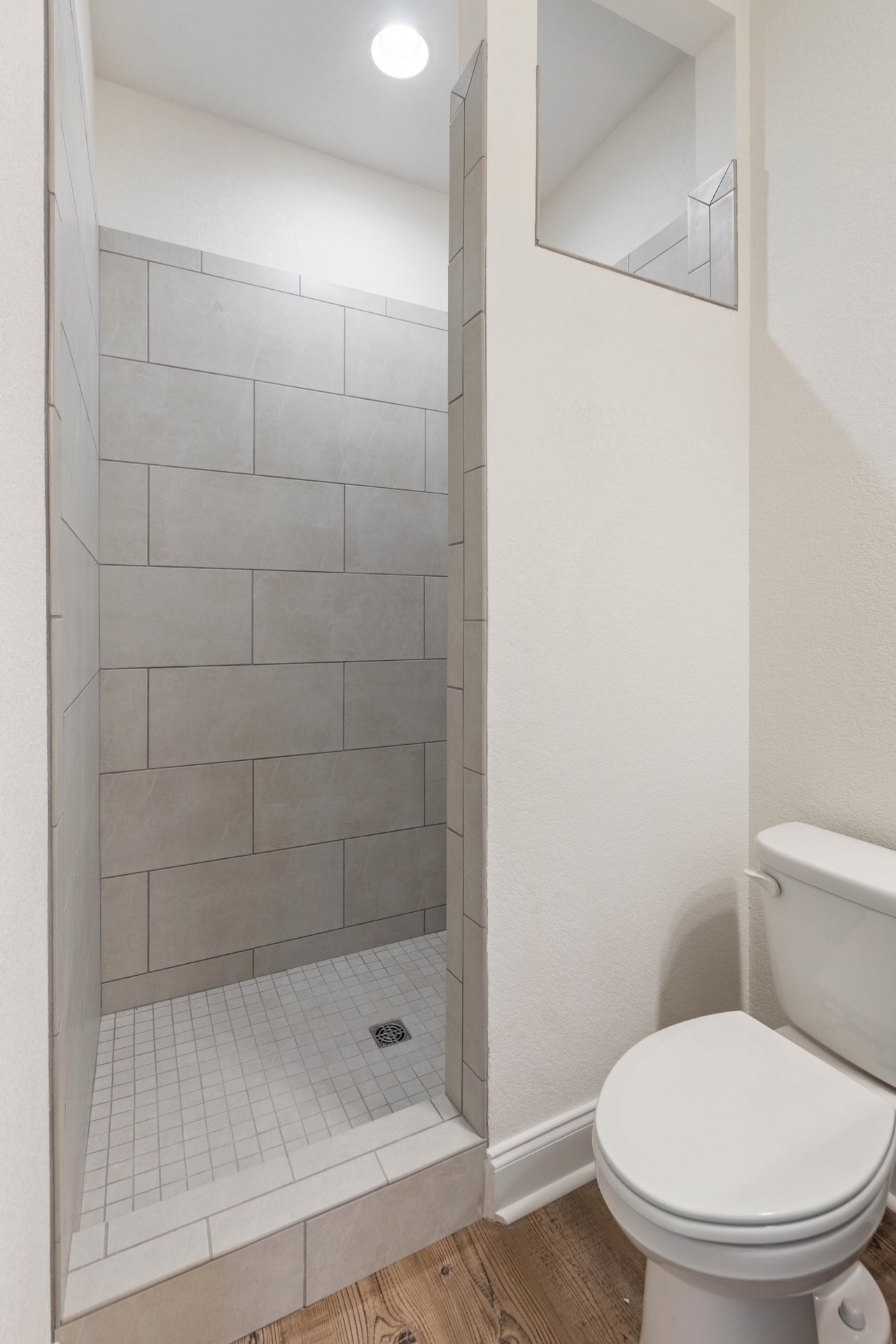 Bathroom with tiled shower, glass door, white toilet with closed lid, wall-mounted mirror, and recessed ceiling light
