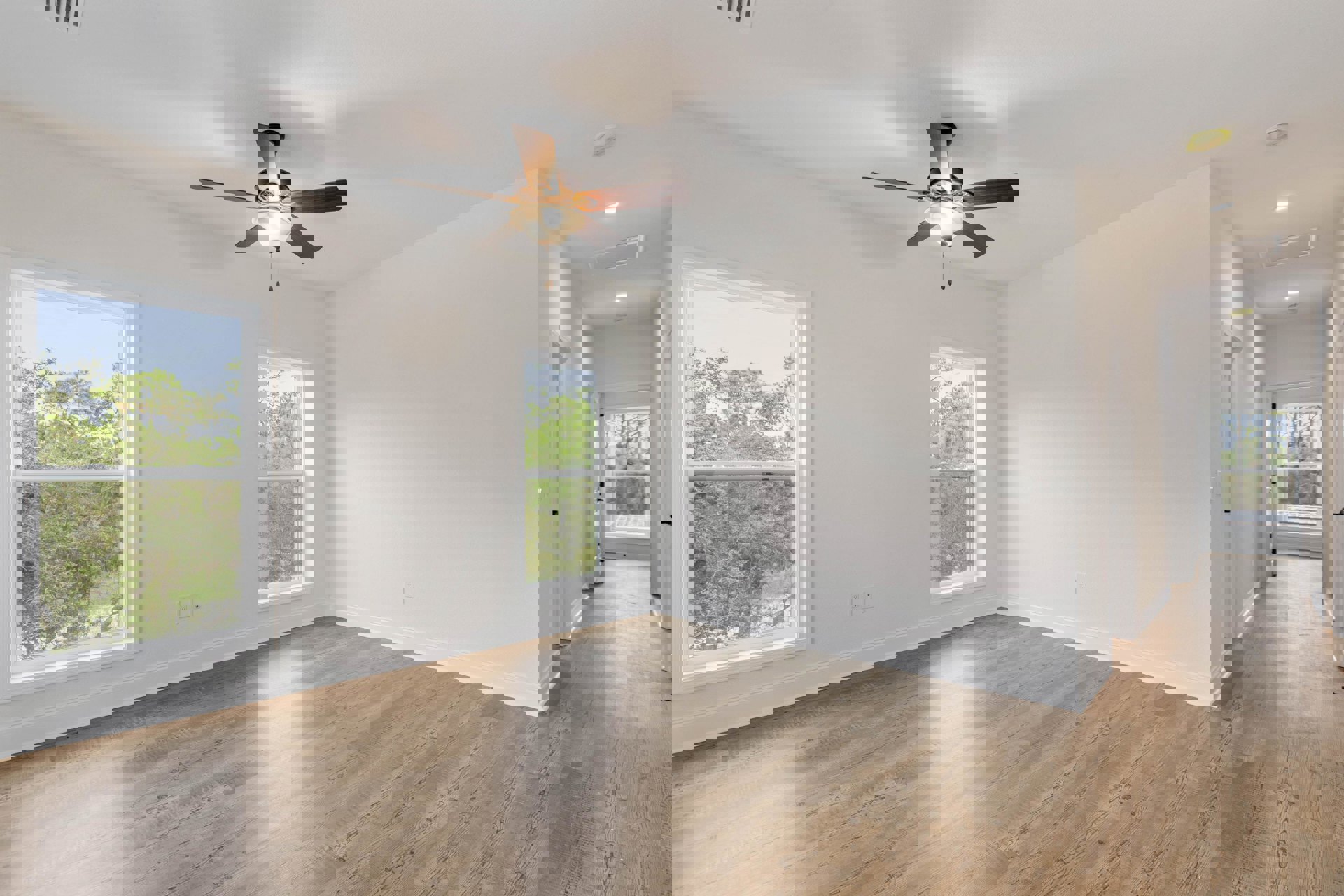 Ceiling fan with light fixture, large windows overlooking trees, wood laminate flooring, white plaster walls