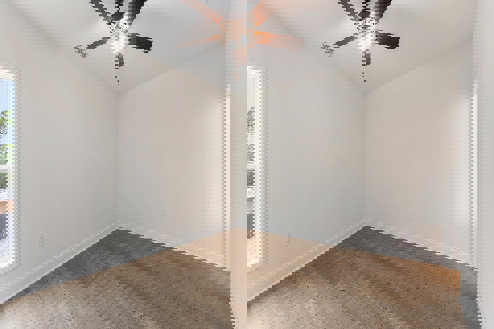 Ceiling fan with light fixture mounted on white plaster ceiling above wood laminate flooring and white walls, window visible in background, air vent nearby