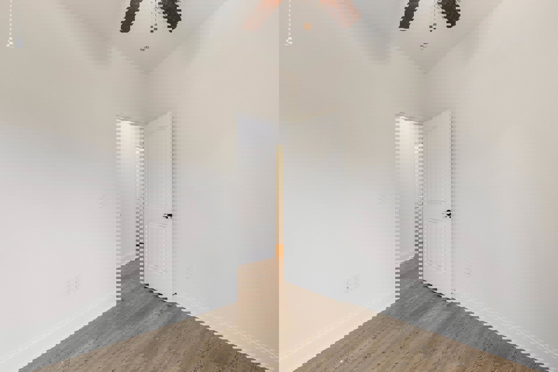 White room with smooth plaster walls, wood flooring, white door with black handle, and ceiling fan with wood blades.