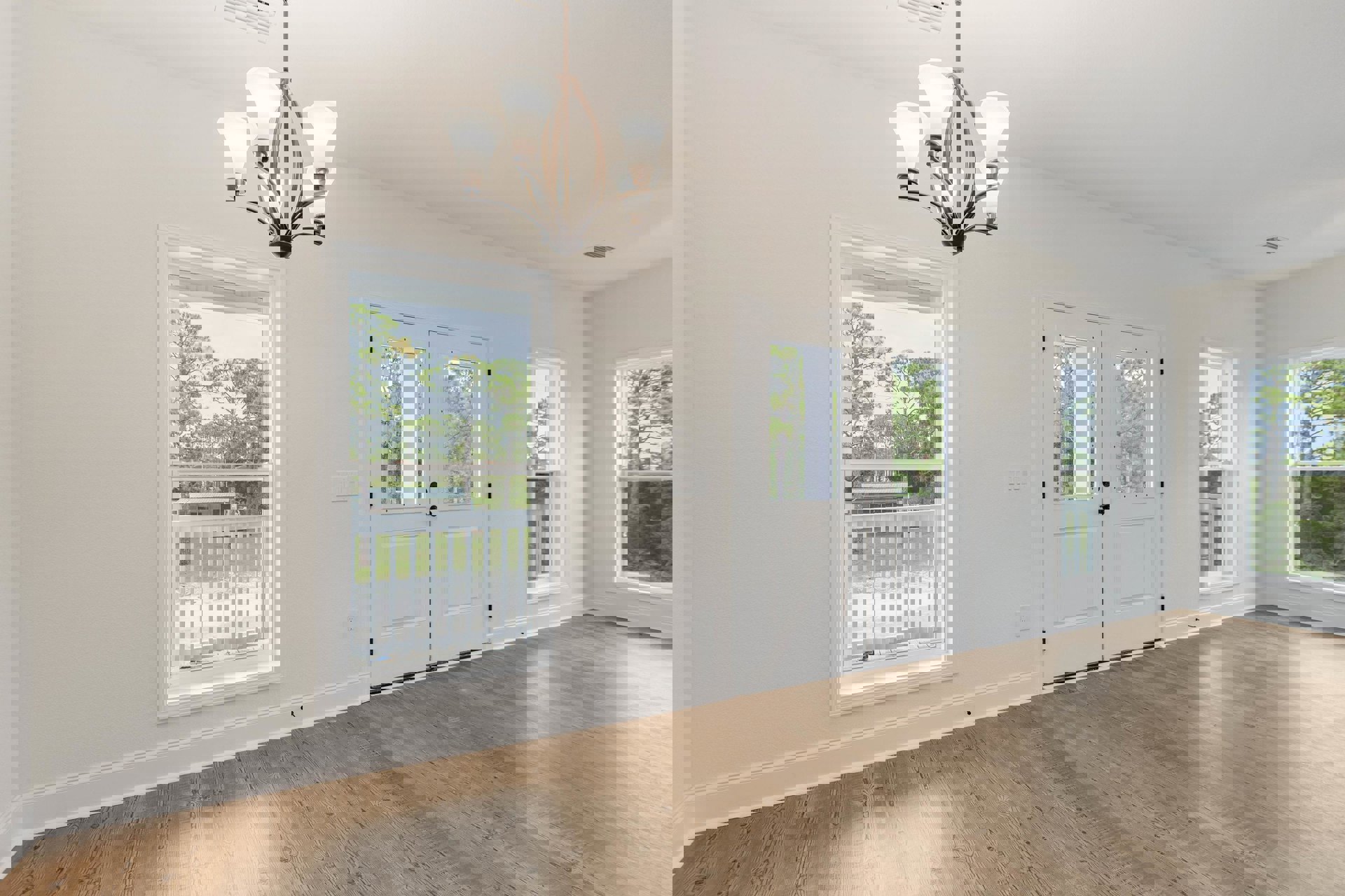 Wood flooring and white walls in a bright room with white doors, windows, and a five-light chandelier; white porch railing visible through the window with trees outside