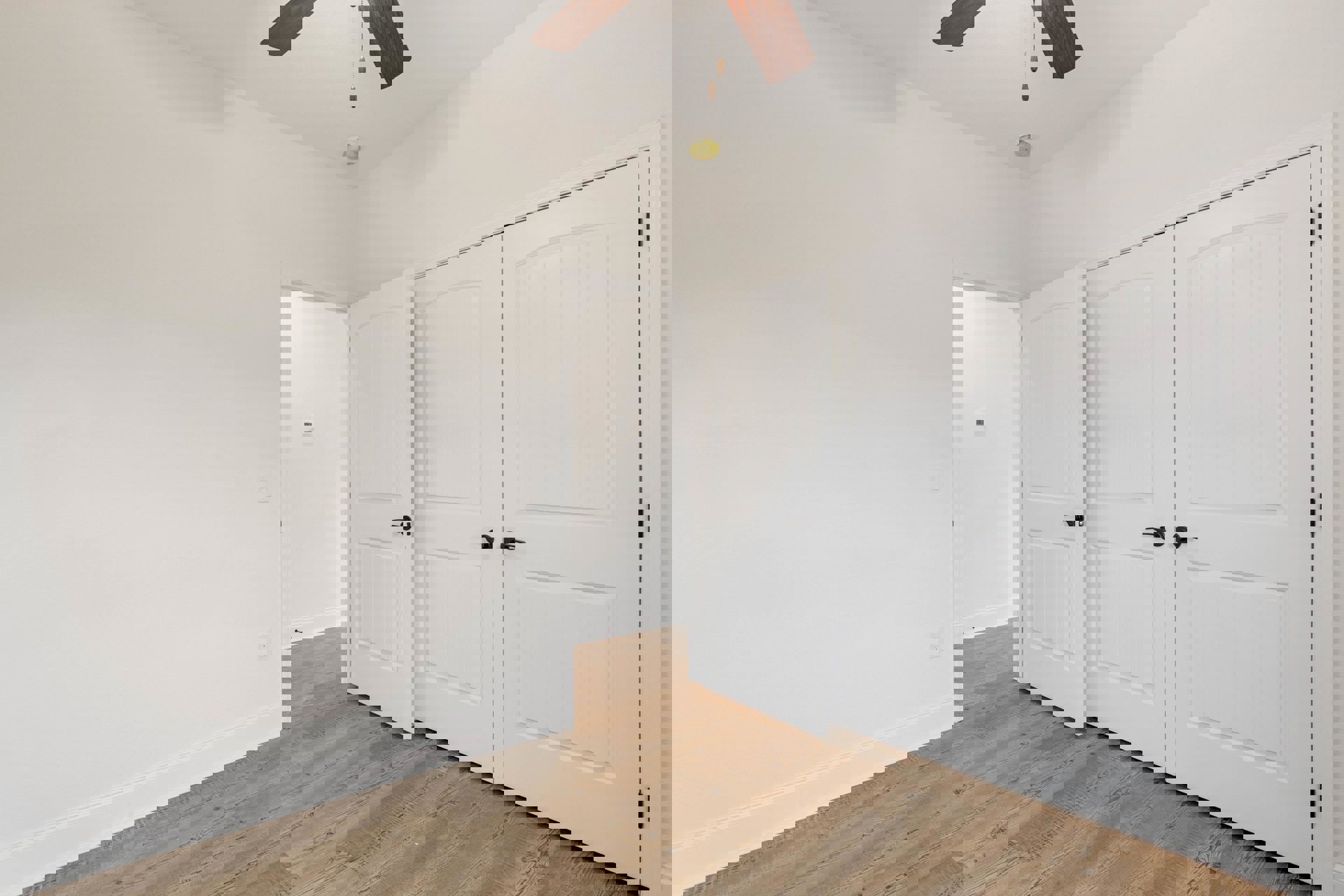 Wood floor and white walls in a room with multiple white doors, black handles, ceiling fan, and a close-up of light-colored curtain.