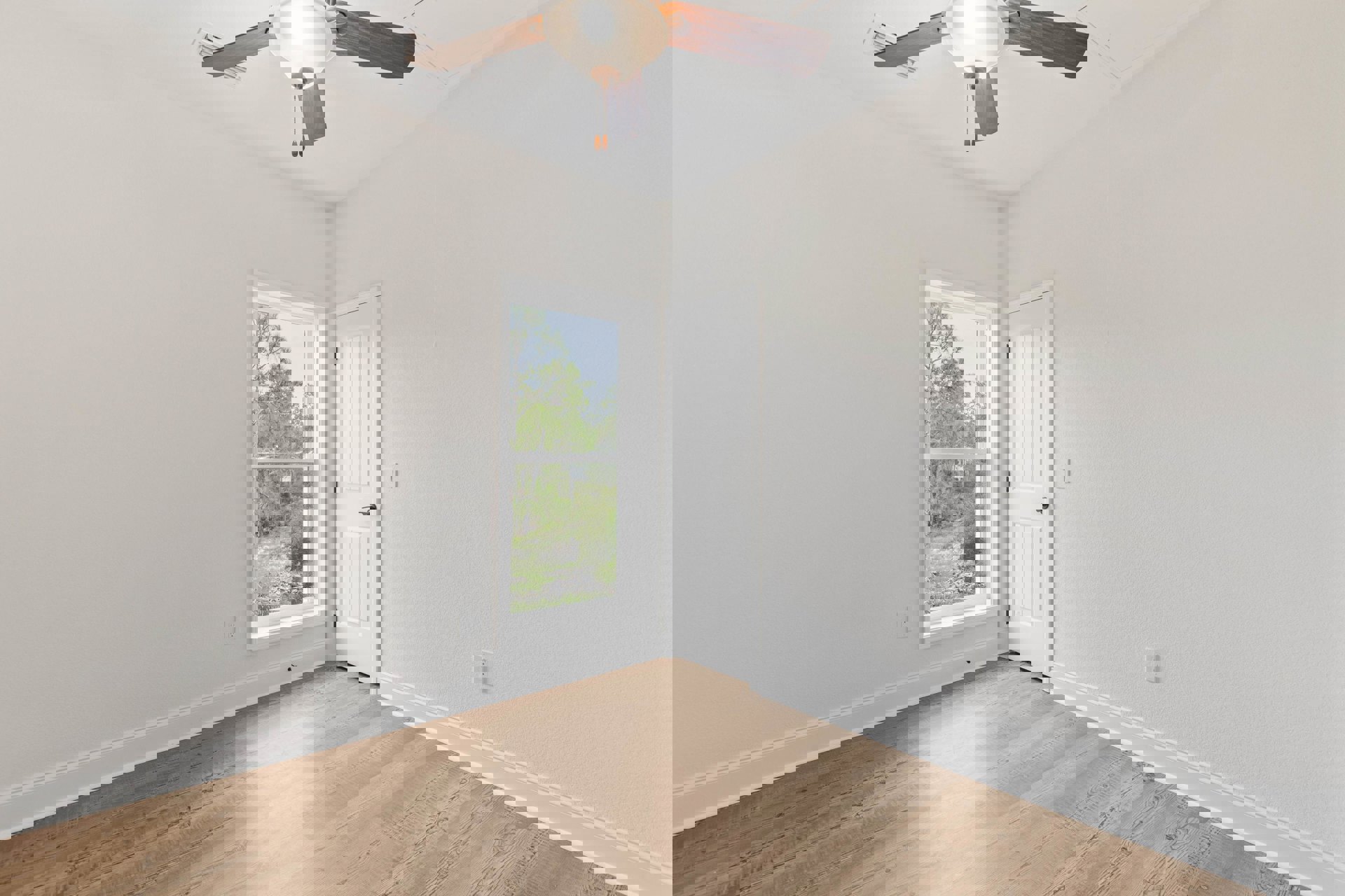 Ceiling fan with integrated light fixture mounted on white plaster ceiling above wood flooring, window with view of trees, and white door in residential room