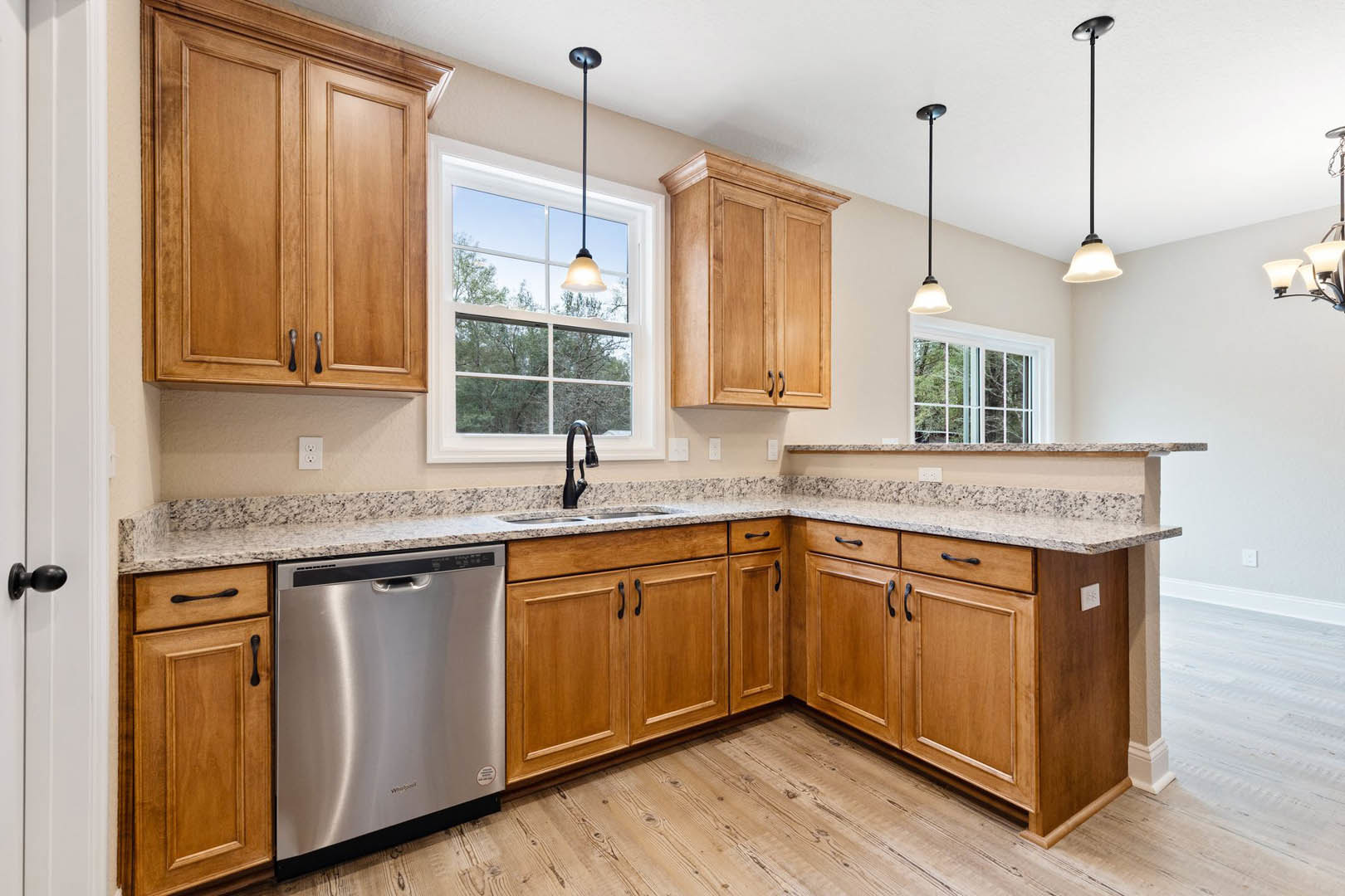 Wooden kitchen cabinets with brushed stainless steel dishwasher, stone countertop, chrome faucet, and pendant ceiling light.