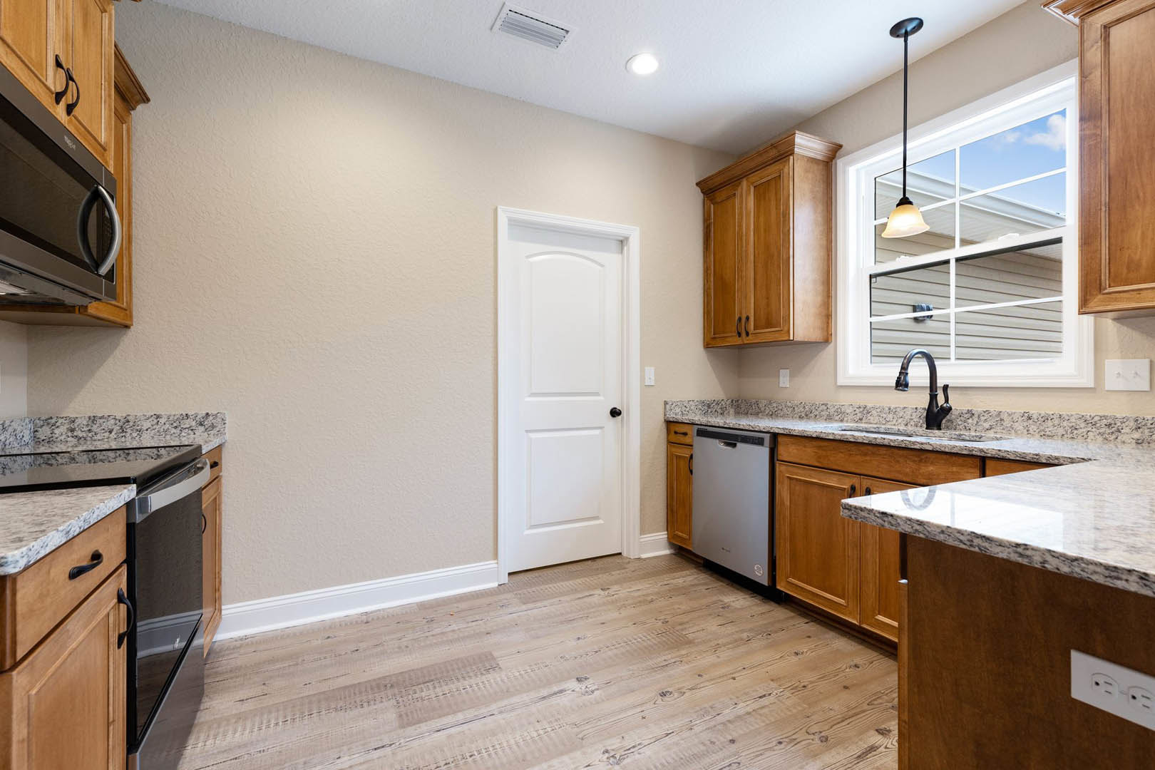 Modern kitchen featuring white cabinetry, stainless steel sink, built-in stove, black hardware, light-colored countertops, and a window allowing natural light.