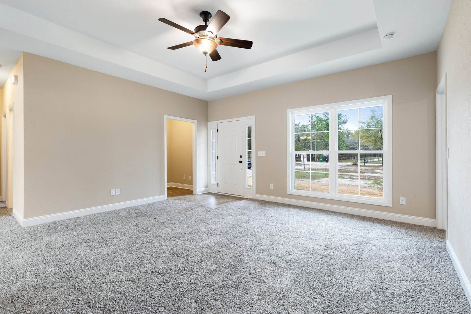 Carpeted room with ceiling fan and light fixture, large window overlooking yard, white door with black knobs, white door frame, light on wall, plaster walls and molding
