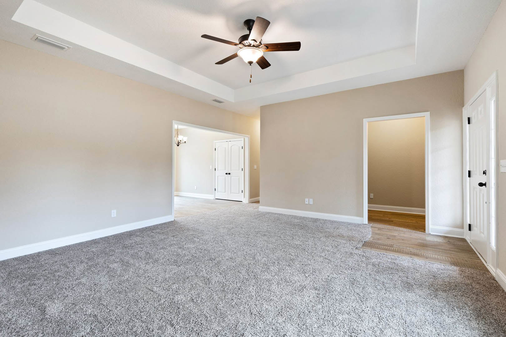 Carpeted room with brown walls, white door frame, white door featuring black handles, ceiling fan with light fixture, white ceiling and molding