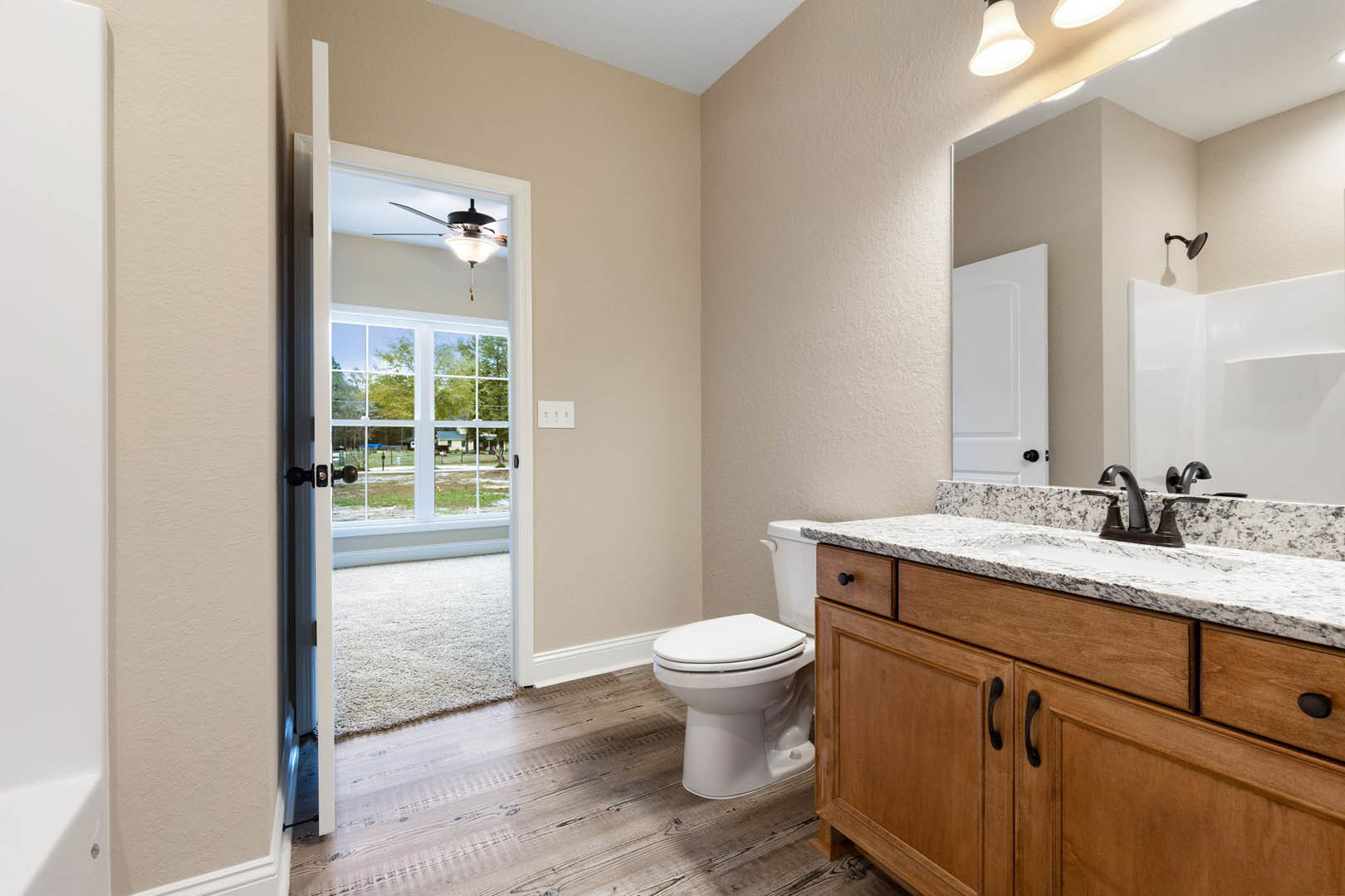 Bathroom with marble countertop sink, white toilet, white walls with brown and white borders, window overlooking yard, tile flooring, modern plumbing fixtures and cabinetry