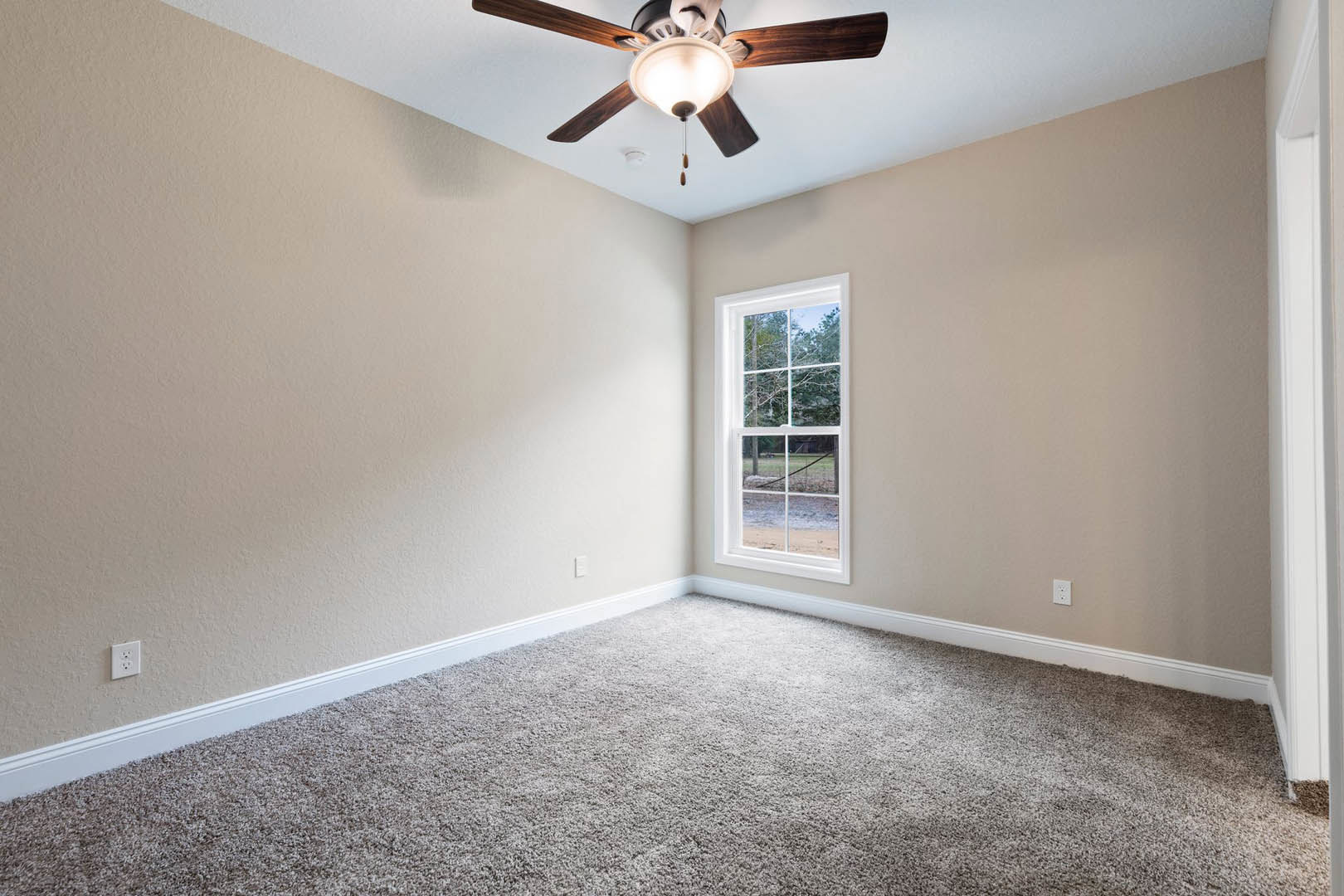 Ceiling fan with integrated light fixture above carpeted floor, window overlooking fenced yard, white plaster ceiling with crown molding