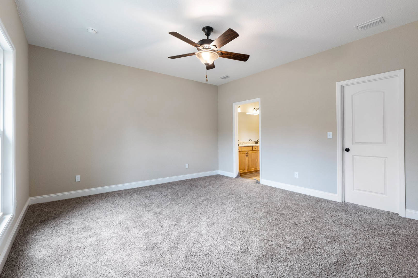 Bedroom with beige carpet, white walls, ceiling fan with light fixture, white door featuring black knob