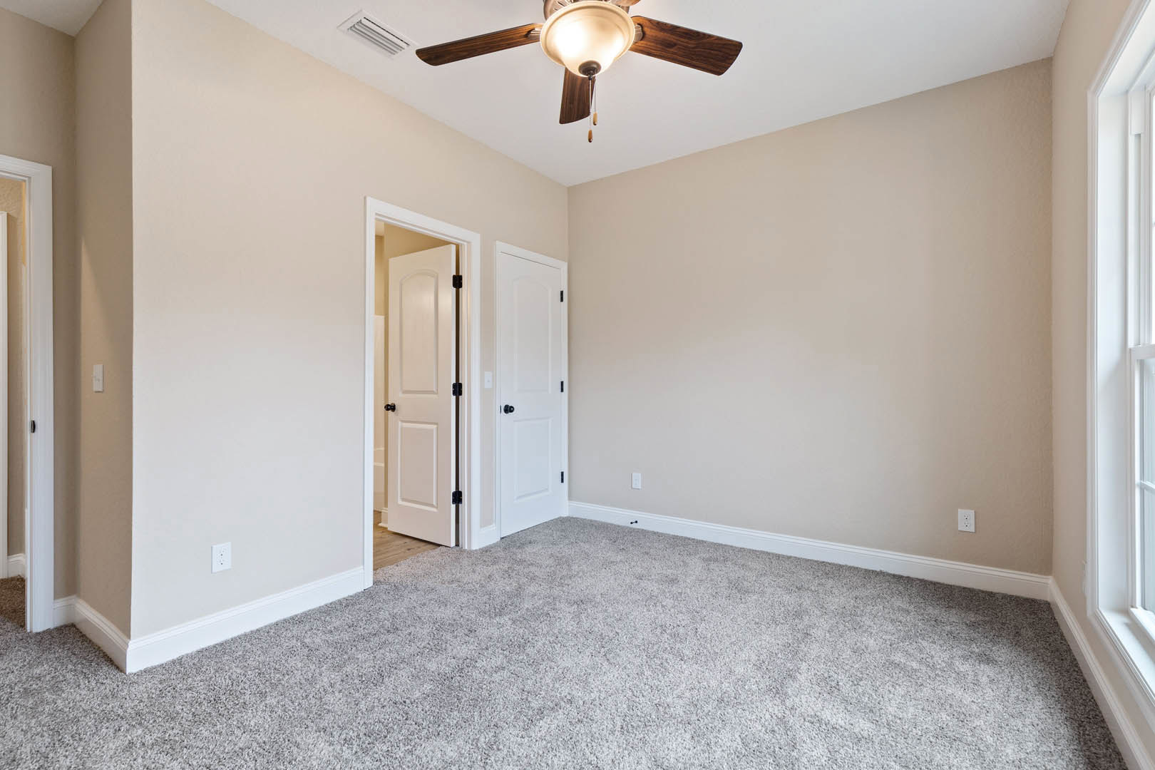 Carpeted room with white paneled door featuring black hardware, ceiling fan with integrated light, white walls, and crown molding.