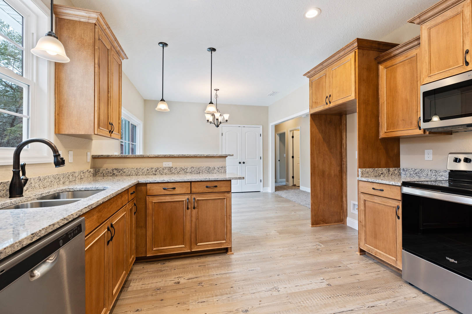 Kitchen with natural wood cabinets, speckled granite countertops, stainless steel microwave and oven, white door with black hardware, chrome faucet, built-in dishwasher