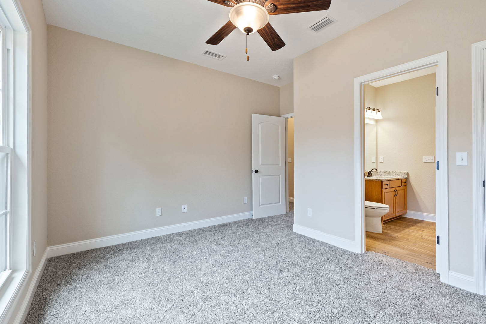 Carpeted room with a ceiling fan and light fixture, open white door with black knob, visible toilet, wooden floor with white rug, plaster walls and molding