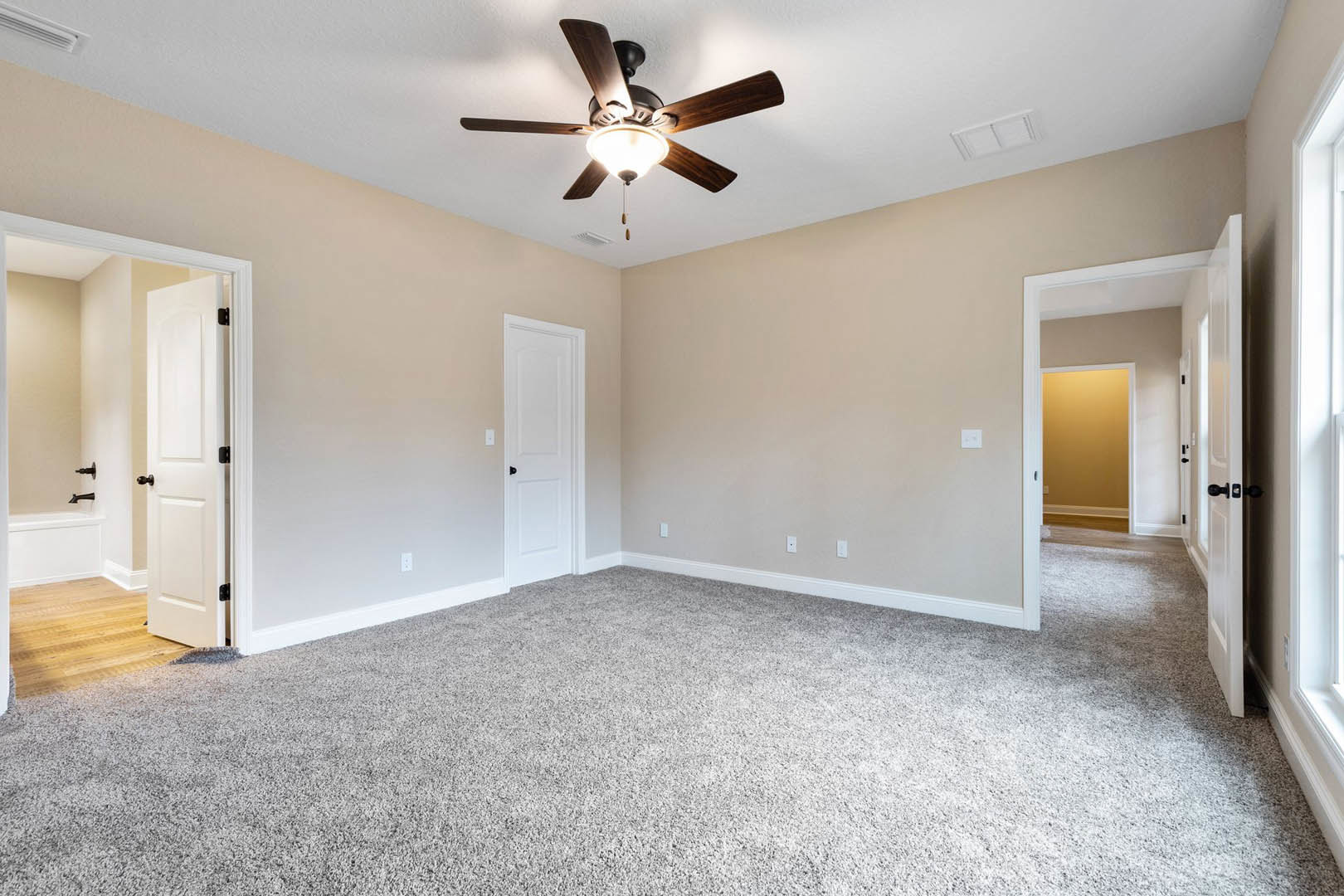 Carpeted room with white walls, ceiling fan with light fixture, white door featuring black knob, simple baseboard molding