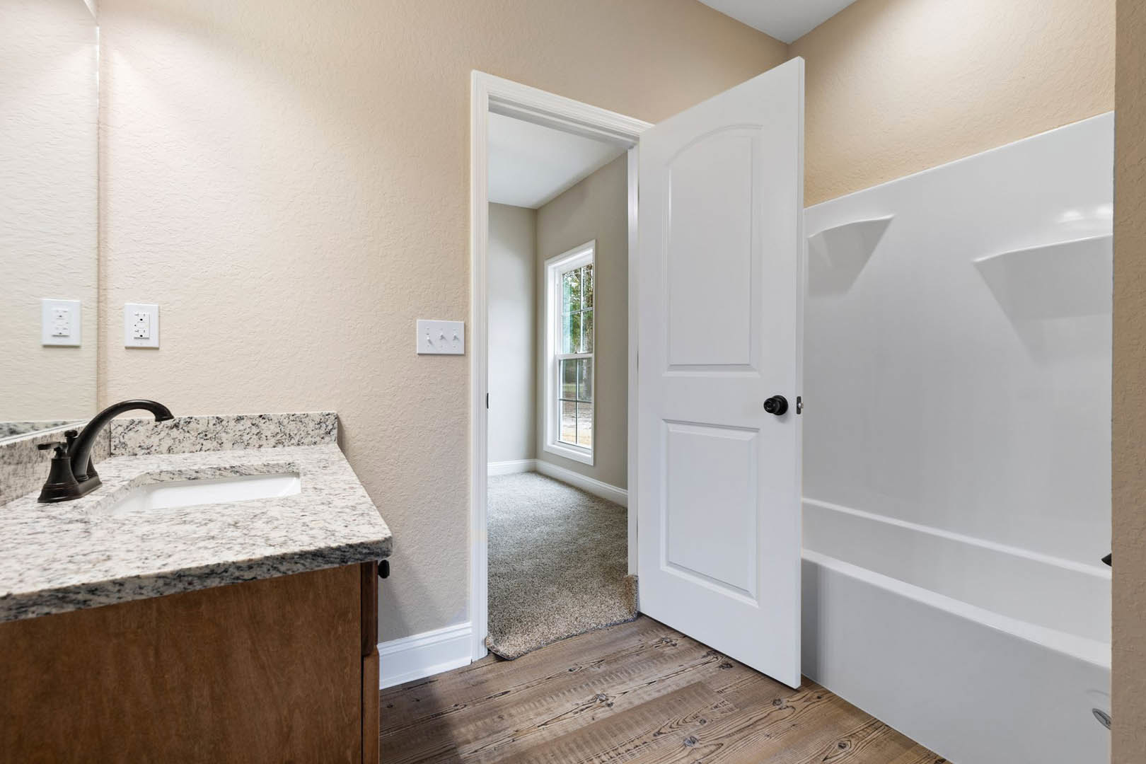 Bathroom with white door, white walls, black hardware, rectangular sink and faucet, white electrical outlet with black switches, light tile flooring