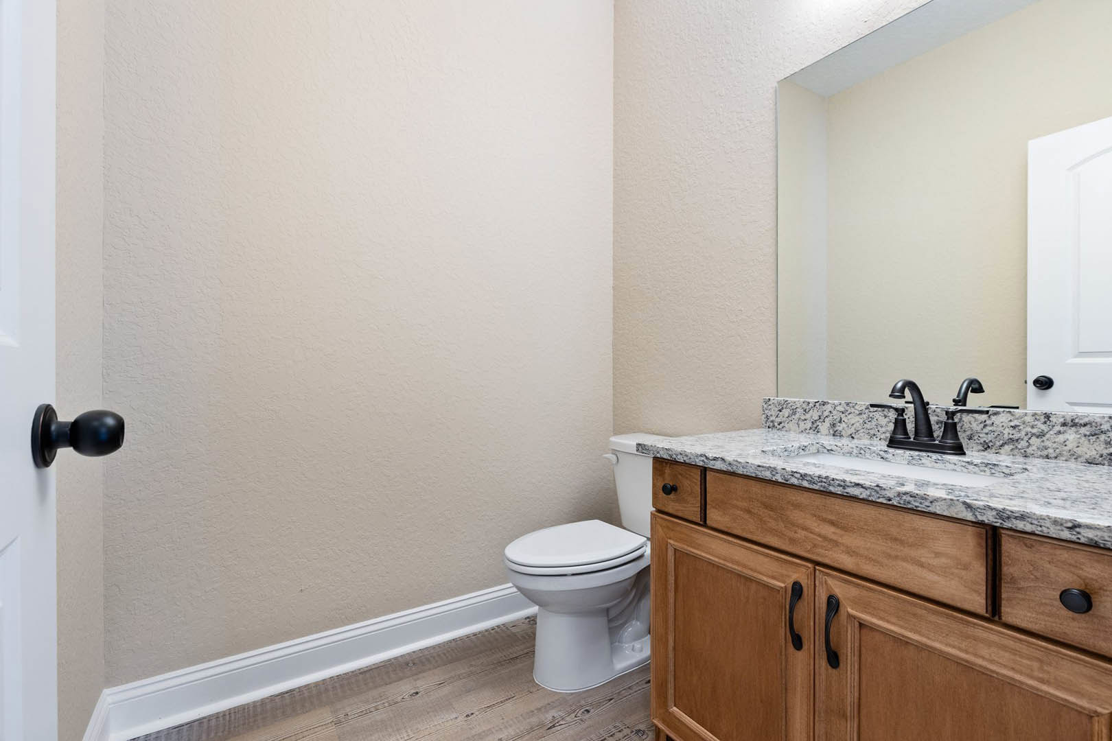 Bathroom with marble countertop, undermount sink, white toilet, chrome faucet, and wall-mounted mirror above light-colored cabinetry