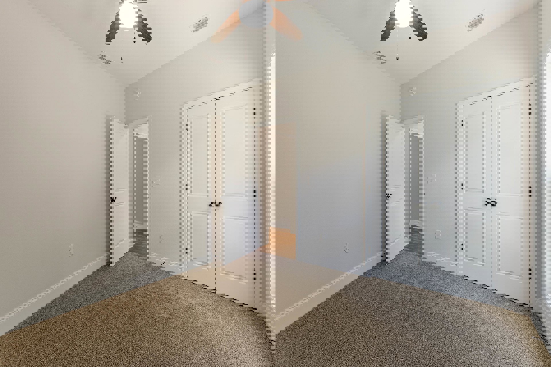 Carpeted room with white double doors featuring black knobs, ceiling fan with light fixture, white walls, and baseboard molding