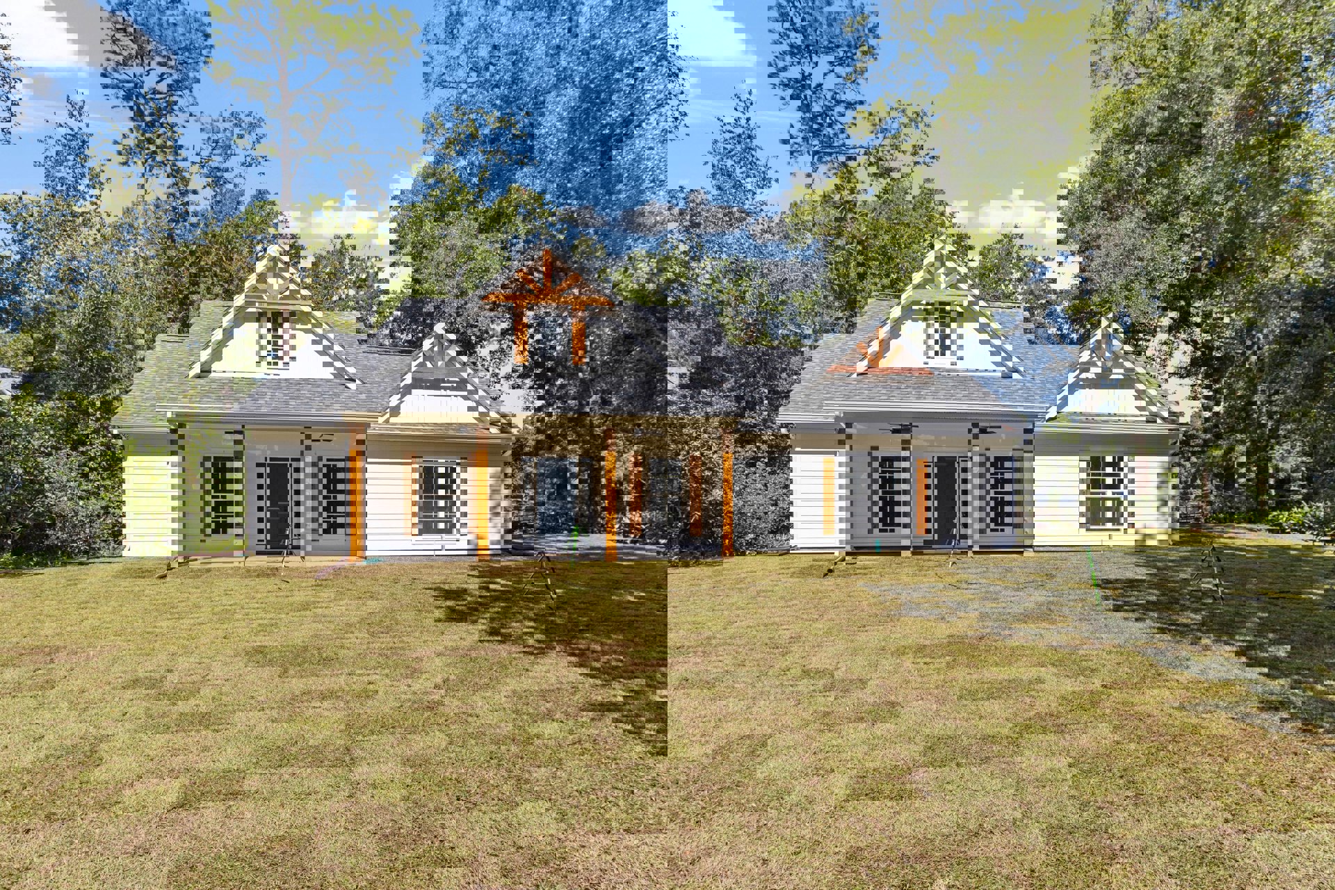 Two-story cottage with white siding, blue front door, white-framed windows, green lawn, mature trees, and a green bicycle near the entrance