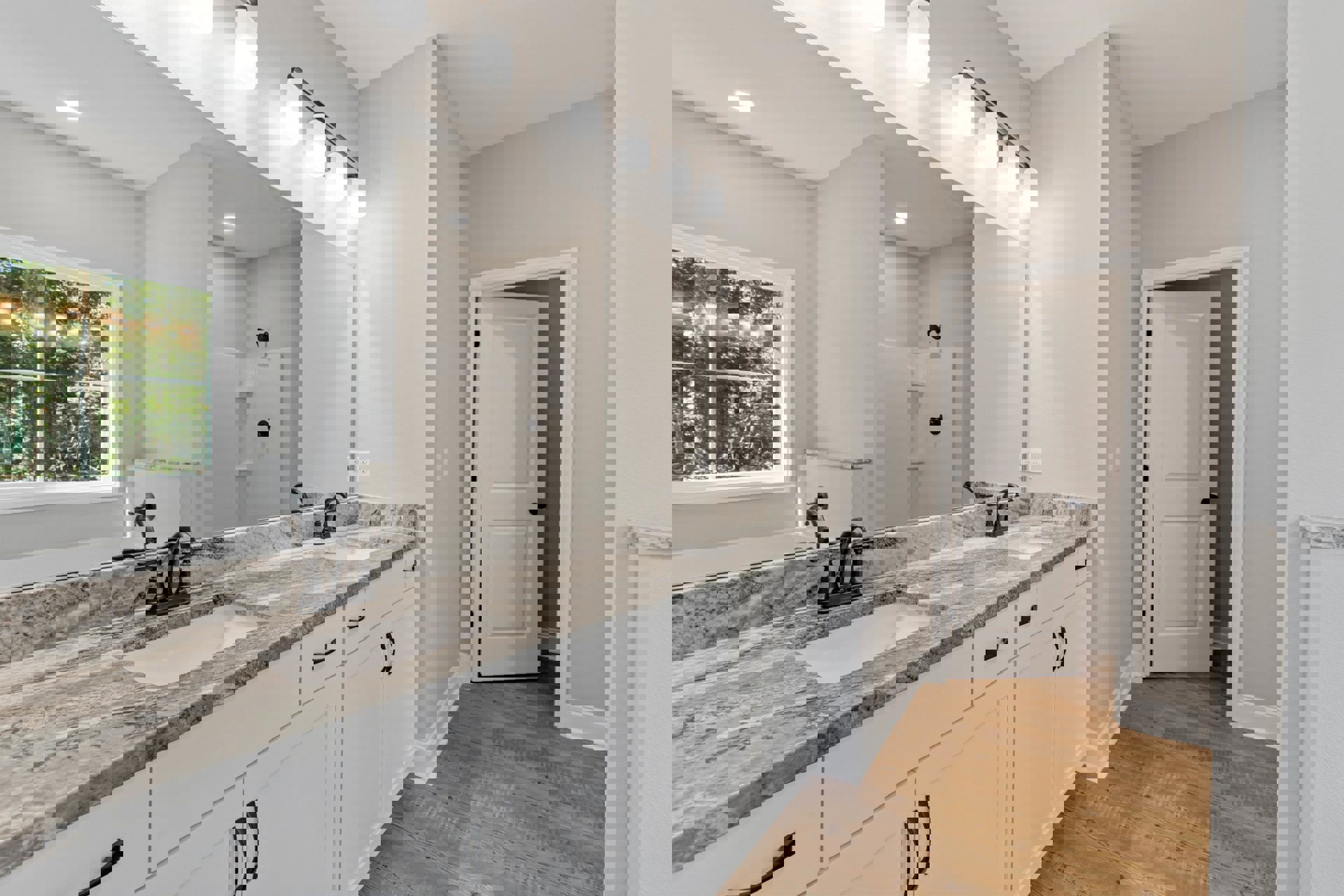 Bathroom featuring a marble countertop, rectangular mirror above the sink, white cabinetry with black knobs, window overlooking trees, and modern light fixture.