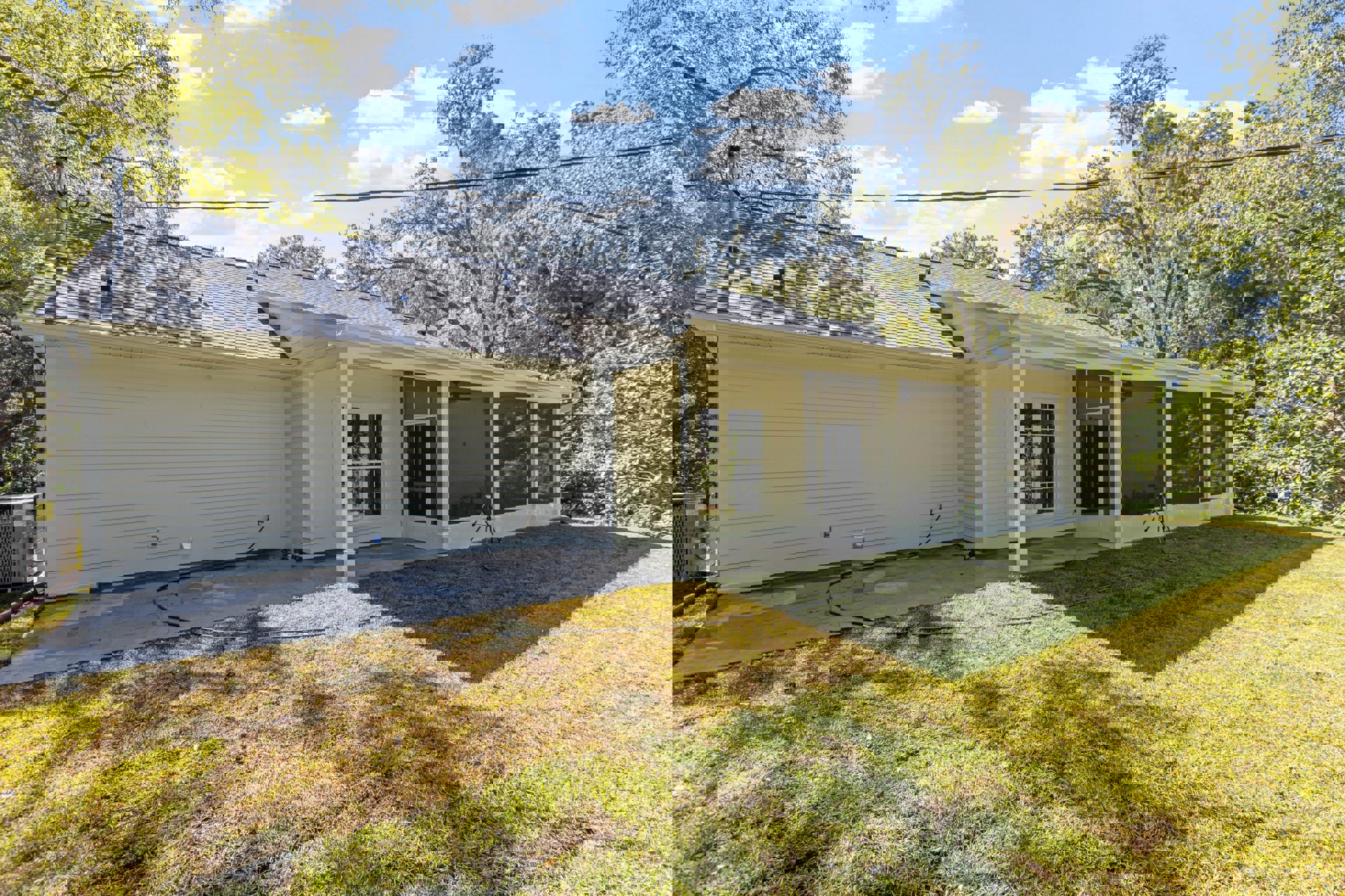 Two-story home with white siding, covered front porch, manicured lawn, mature trees, and black screened windows