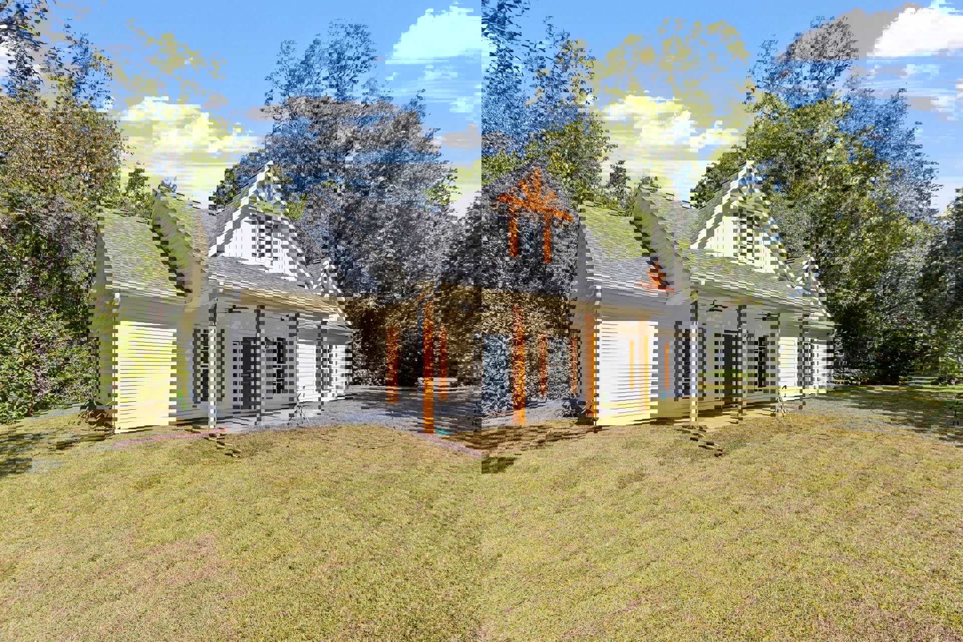 White siding home with blue front door, black-trimmed windows, attached white garage door, manicured green lawn, mature trees in background, partly cloudy sky overhead.