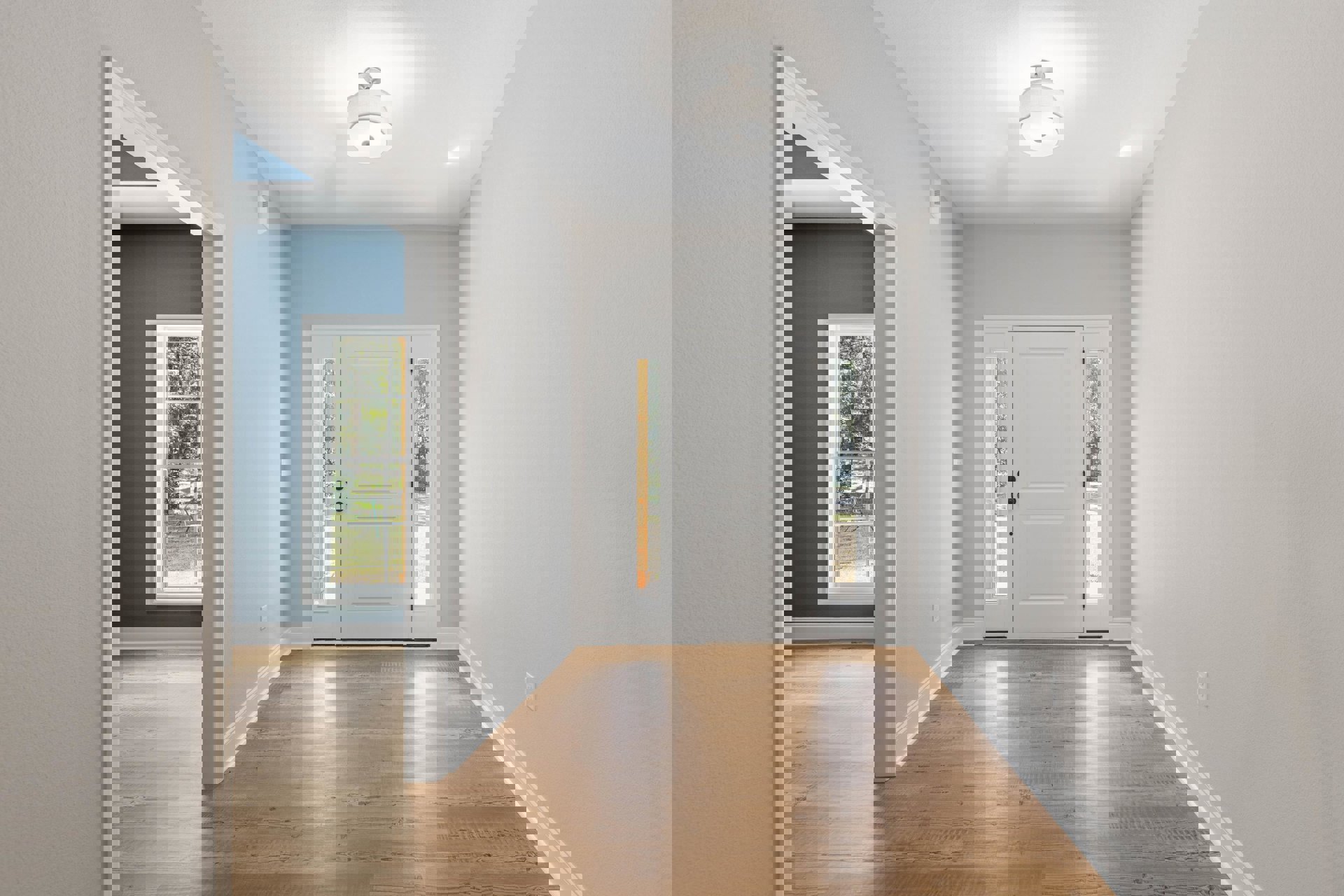 Hallway with wood flooring, white door featuring glass panes and black knobs, white walls with molding, light fixture with white shade, window overlooking forest.