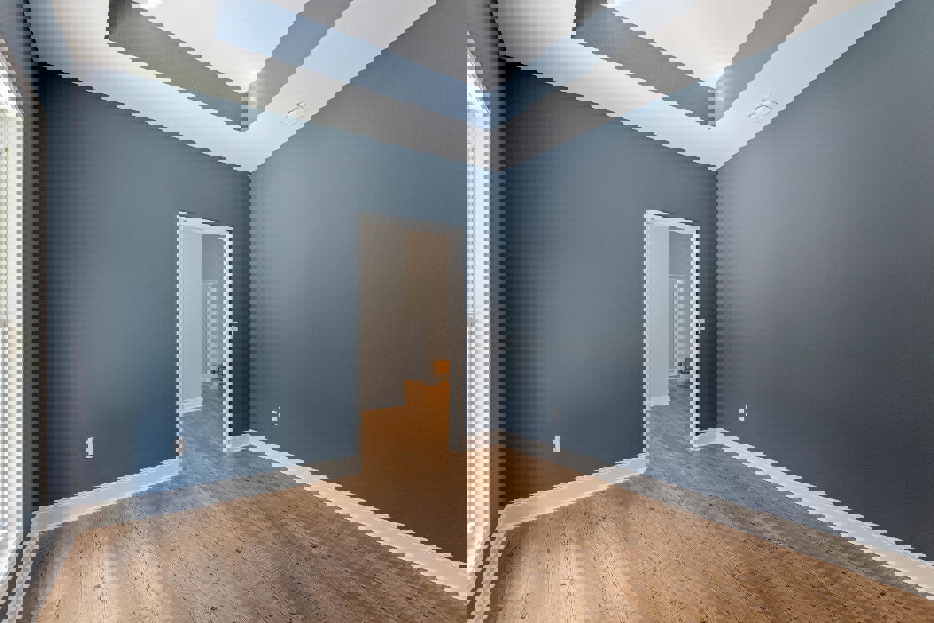 Open white door leading into a room with wood flooring, white walls, white ceiling vent, and blue ceiling accents