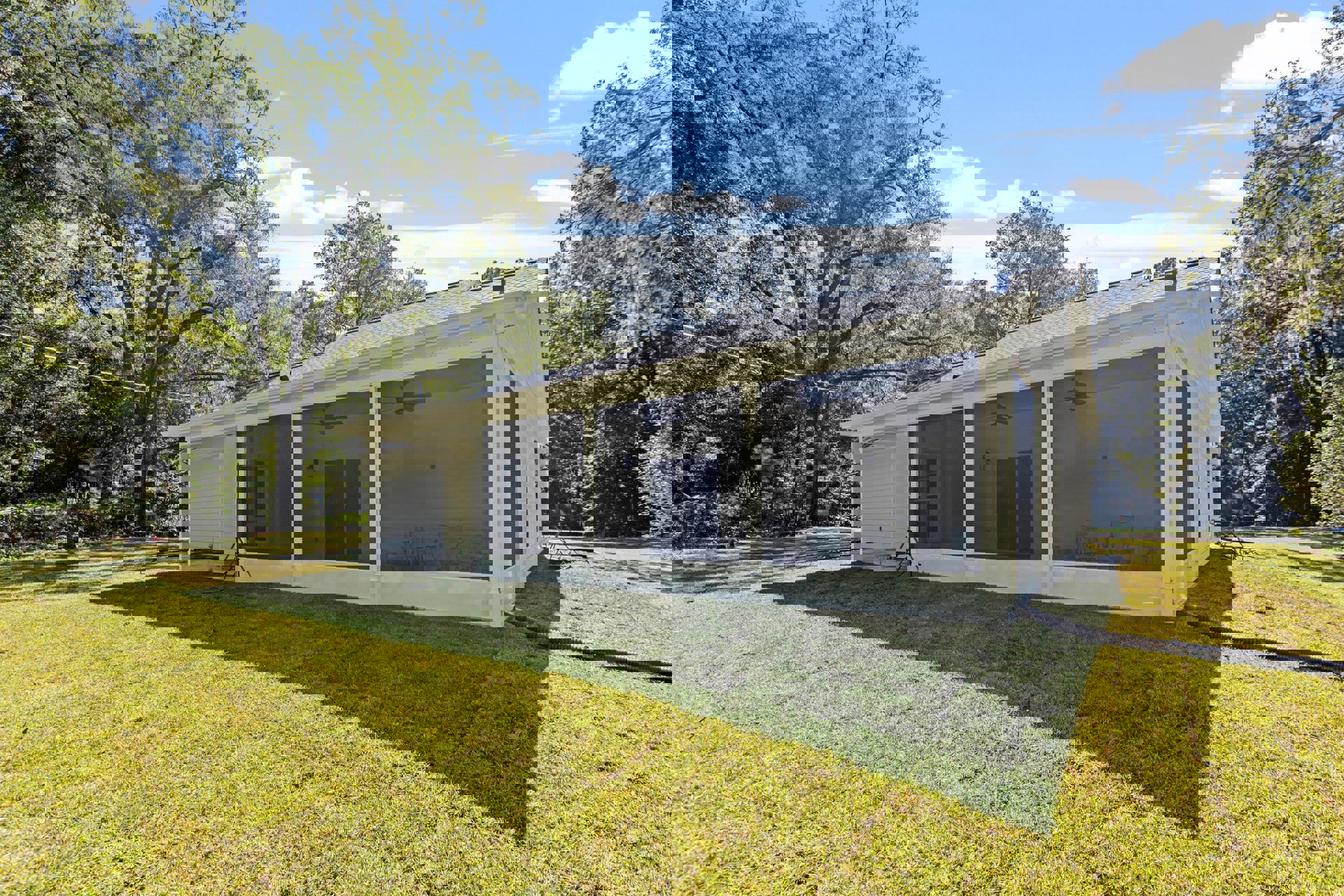 White house with screened porch, white trim, screen door, grassy lawn, black metal pipe, trees and clouds in background