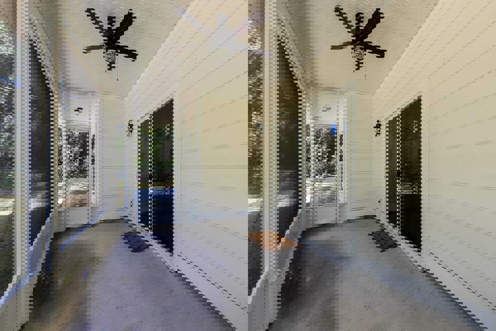 Screened porch with concrete floor, brown welcome mat, ceiling fan with light, and white screen door leading indoors