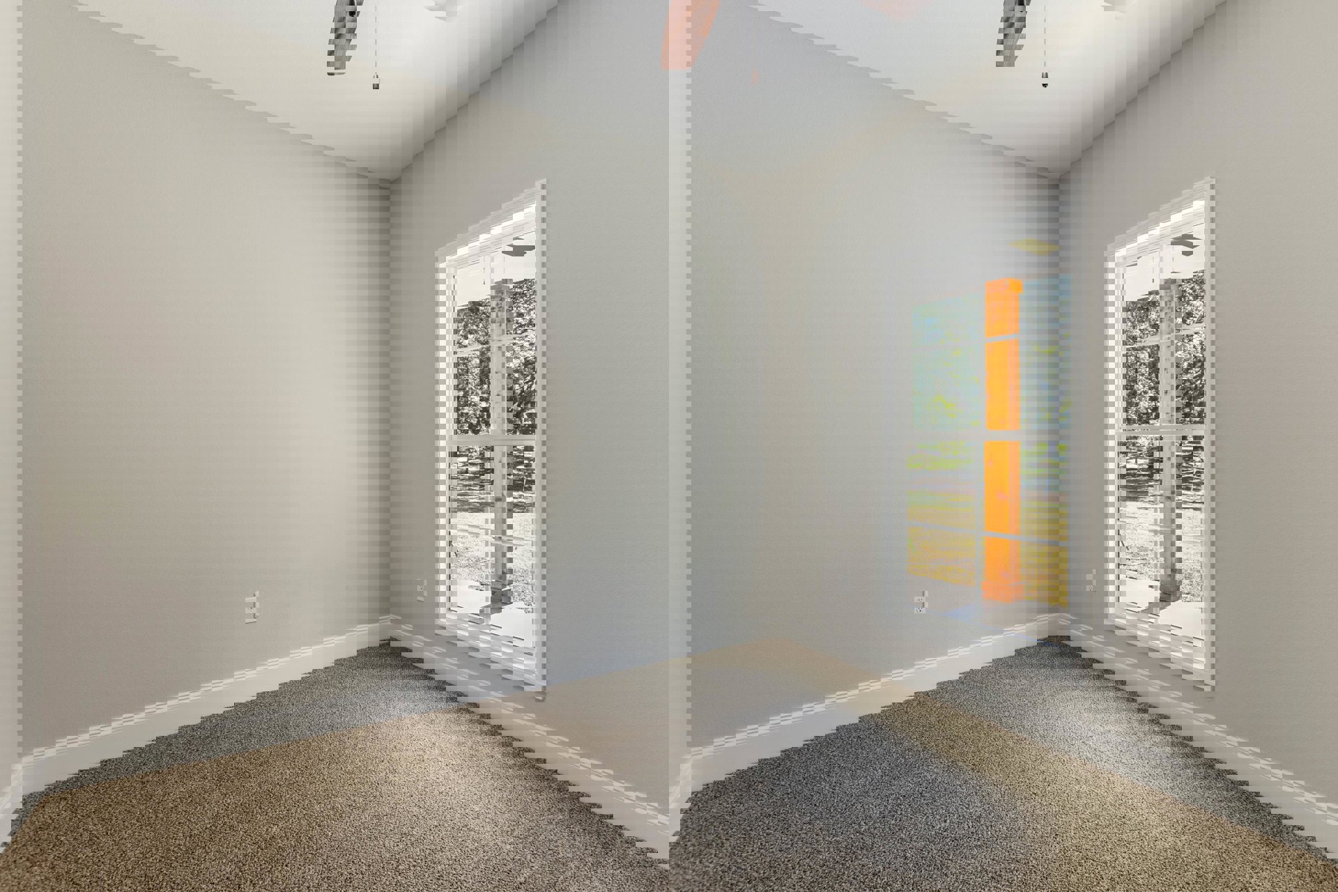 Carpeted room with large window framed by wood trim, ceiling fan with pull chain, and view of trees outside